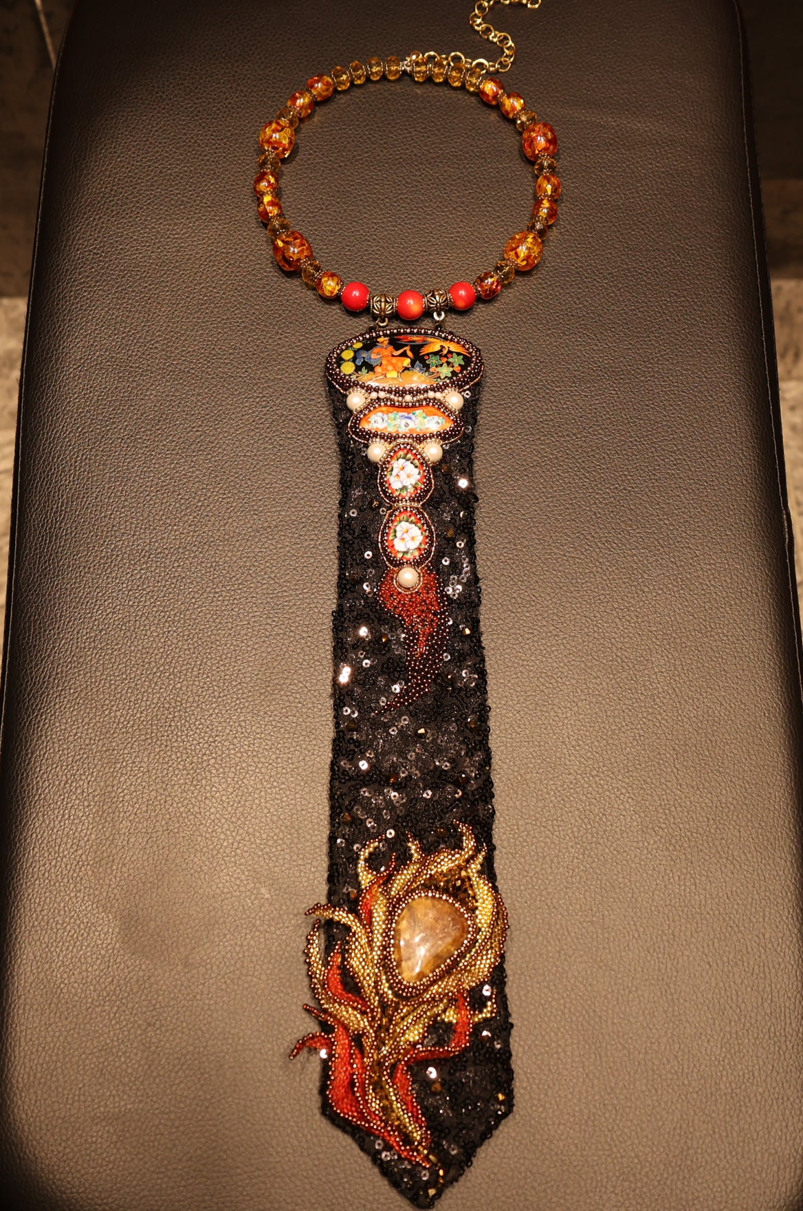 CRAVATTA GIOIELLO realizzata interamente a mano con la tecnica del ricamo a rilievo, ispirata alla creatura folkloristica 
"L'uccello di Fuoco".
Cristalli di vetro, Smalto, Perle di vetro, Coralli di vetro, Perle Swarovski, Perline, Paillettes, Pietra di calcite giallo/miele, 
4 Dipinti in miniatura laccati (l'Uccello di Fuoco e 3 floreali)